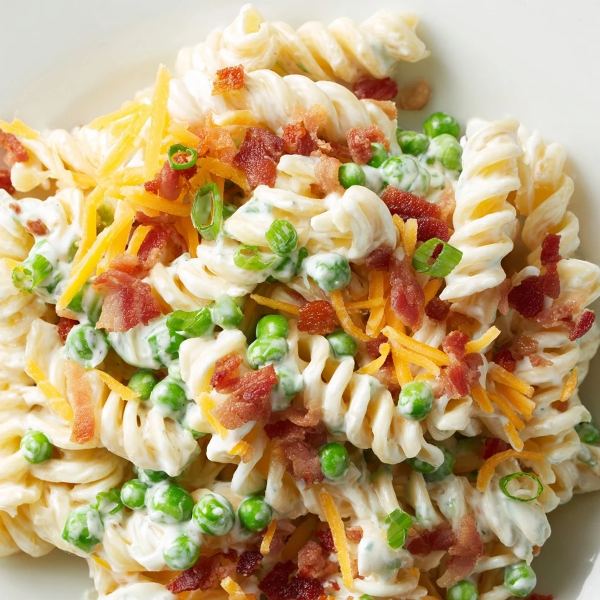Colorful American pasta salad featuring rotini noodles, green onions, peas, and melted cheese coating.