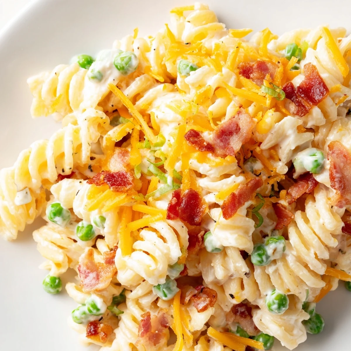Cold pasta side dish with bacon crumbles, cheddar cheese, and creamy ranch dressing garnished with green onions.