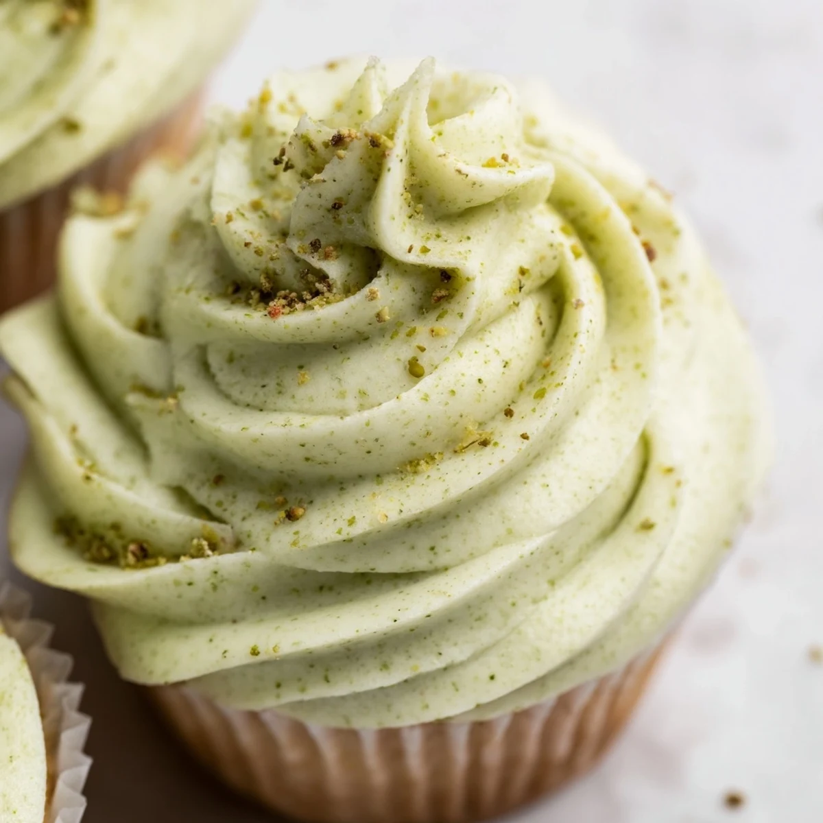 Moist pistachio cupcakes served on a white plate, crowned with fluffy buttercream and delicate nut sprinkles.