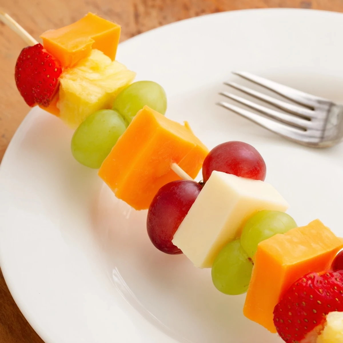 Colorful fruit and cheese kabobs arranged on a white platter with fresh mint garnish