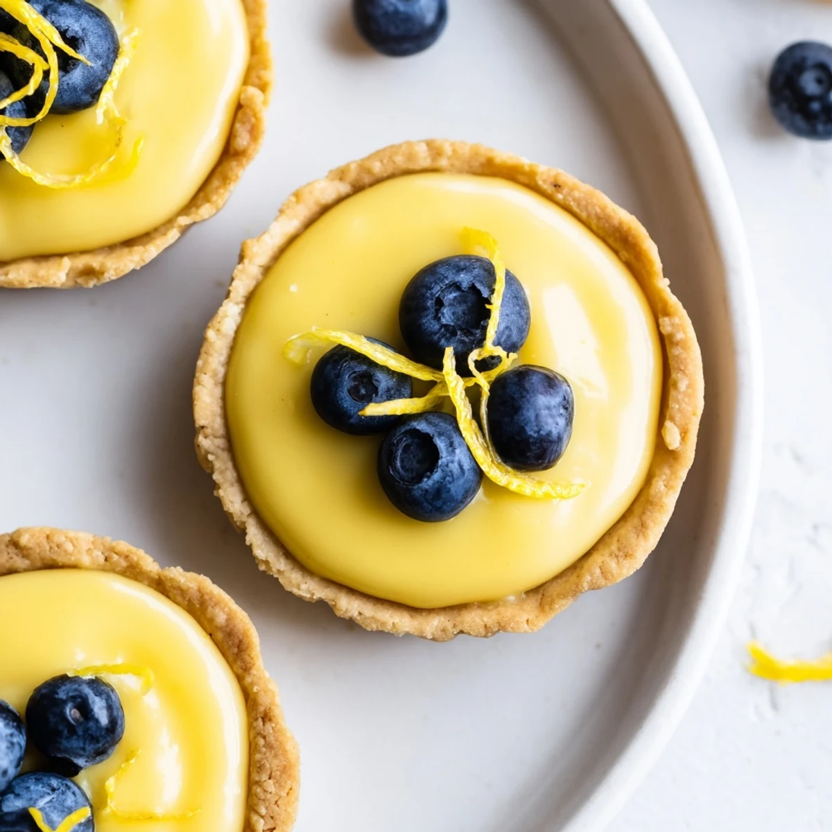 Golden mini vegan lemon tarts topped with fresh berries on a rustic white plate
