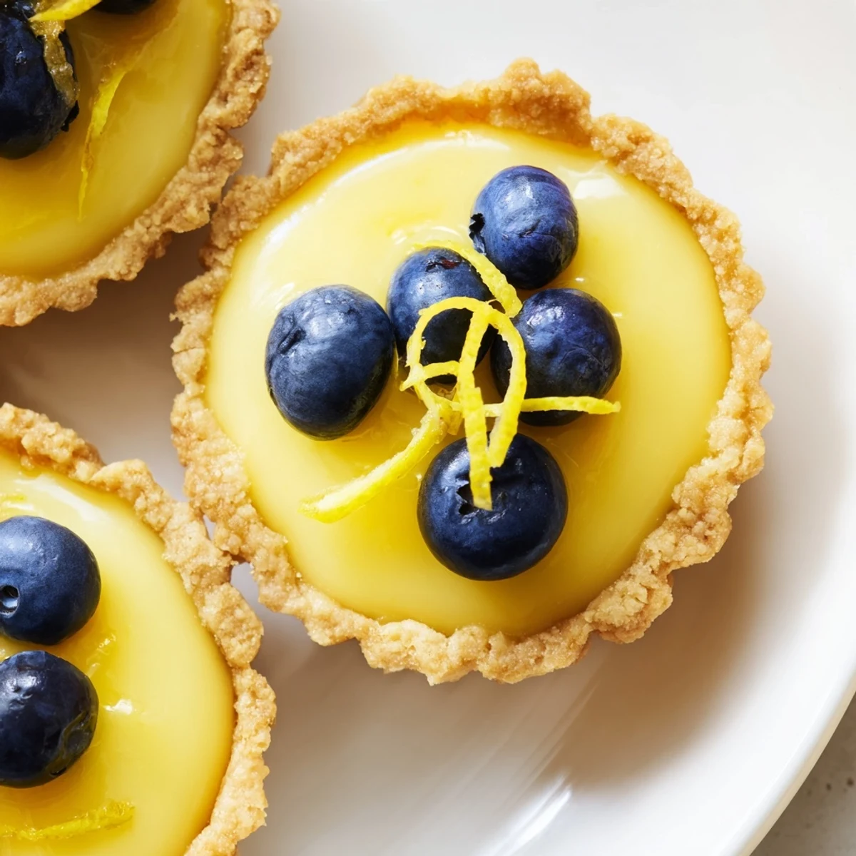 Creamy mini vegan lemon tarts in crisp almond crusts garnished with delicate lemon zest