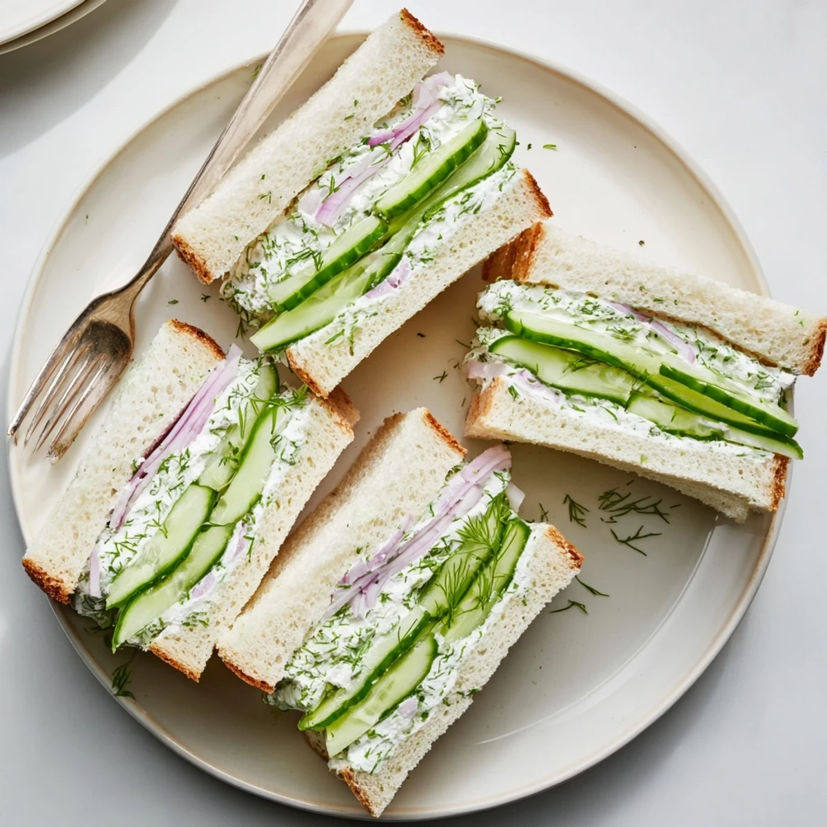 Creamy cucumber salad sandwiches stacked with thin cucumber slices on whole wheat bread, served on a wooden board for entertaining.