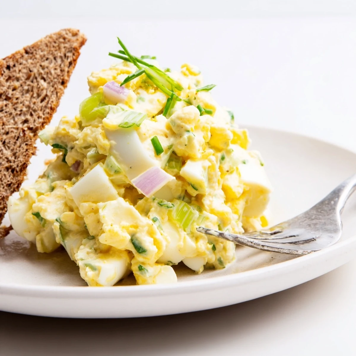 Silky Classic Egg Salad Recipe piled on toasted rye, chives sprinkled on top