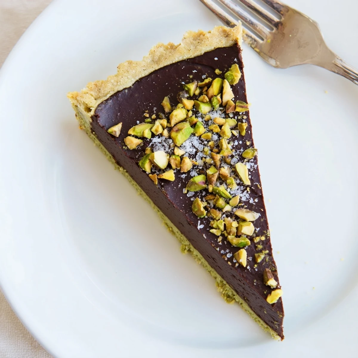 Glossy dark chocolate pistachio tart topped with crushed nuts and flaky sea salt