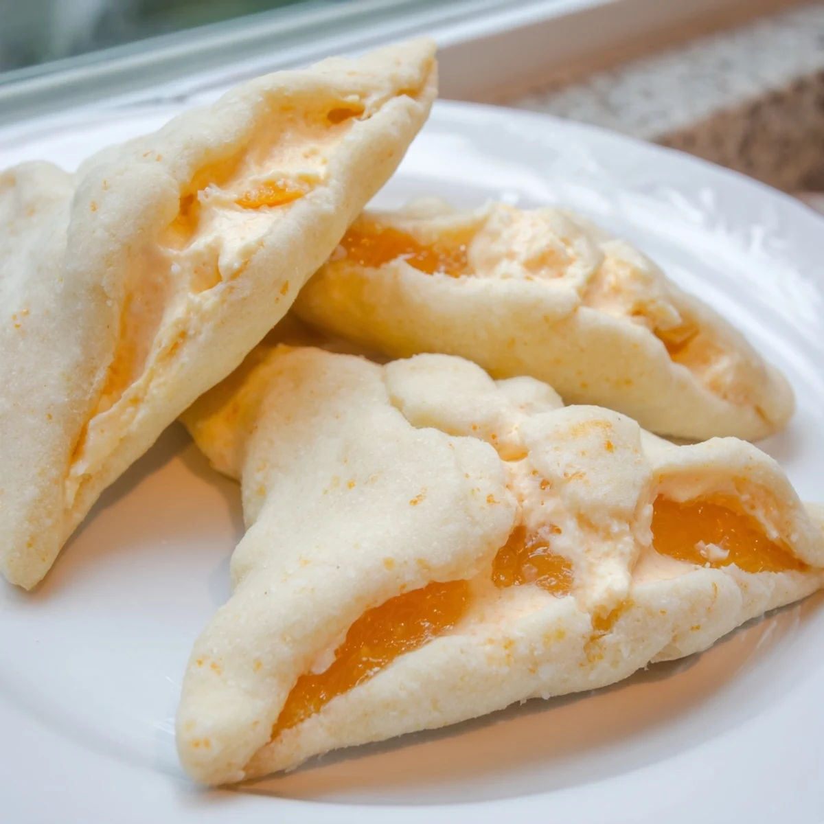 Triangular creamsicle hamentaschen dusted with sugar filled with bright citrus cream
