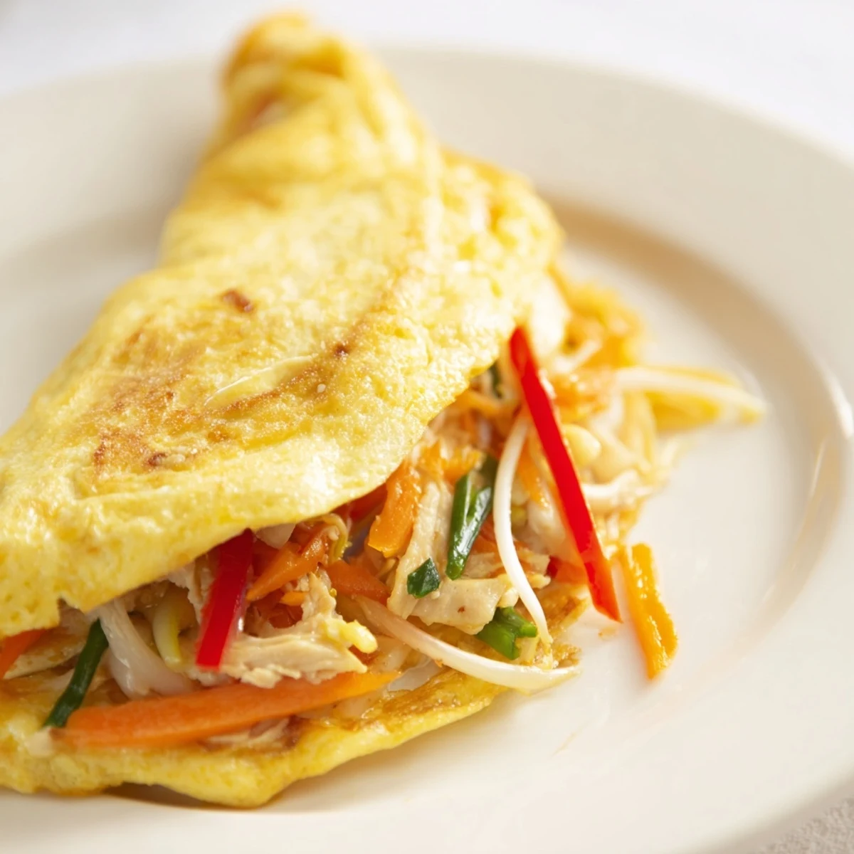 Golden Chinese omelette folded over tender chicken and crisp colorful vegetables on a plate